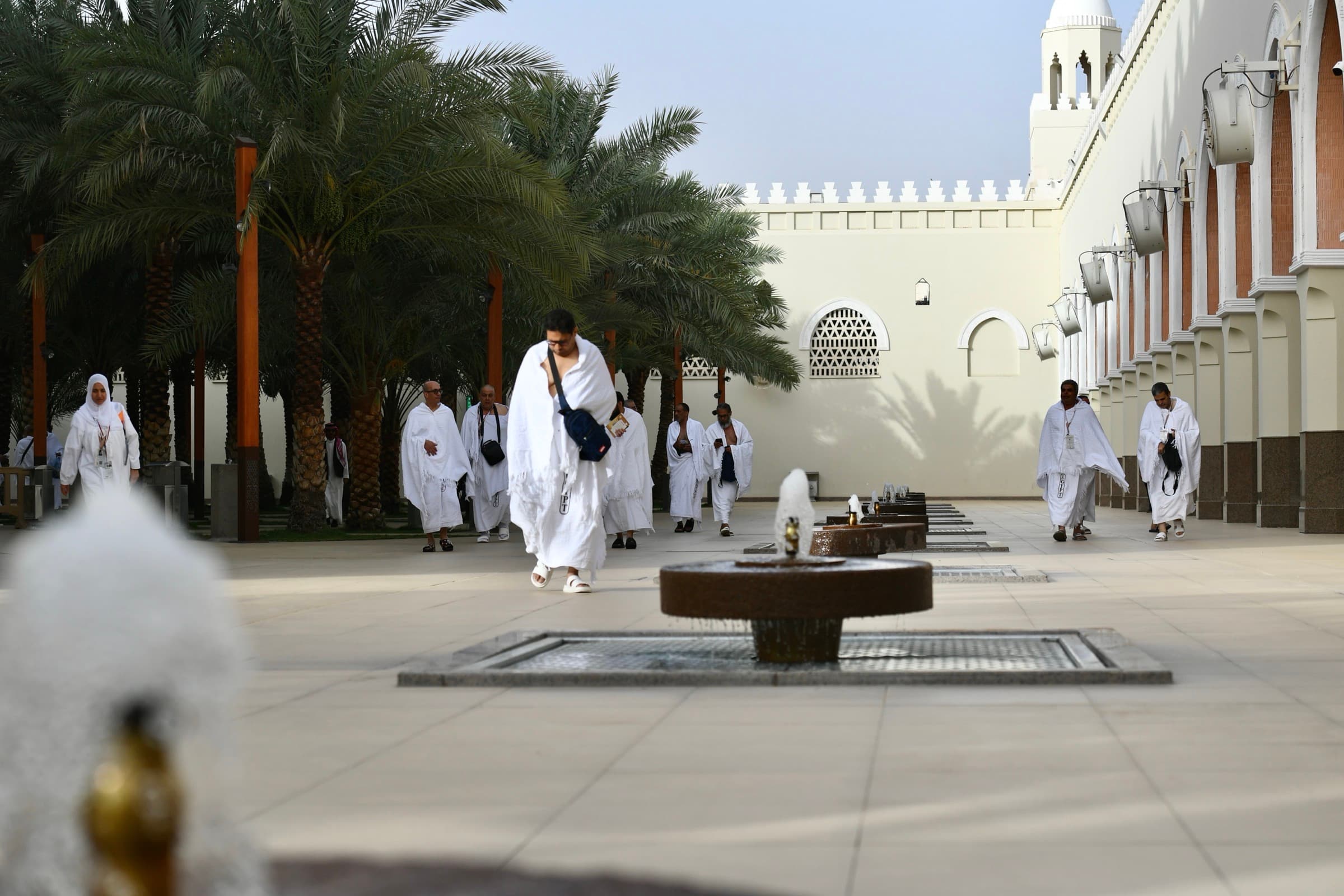 Hero: pilgrims in ihram walking through a Miqat mosque courtyard, on their way to Makkah