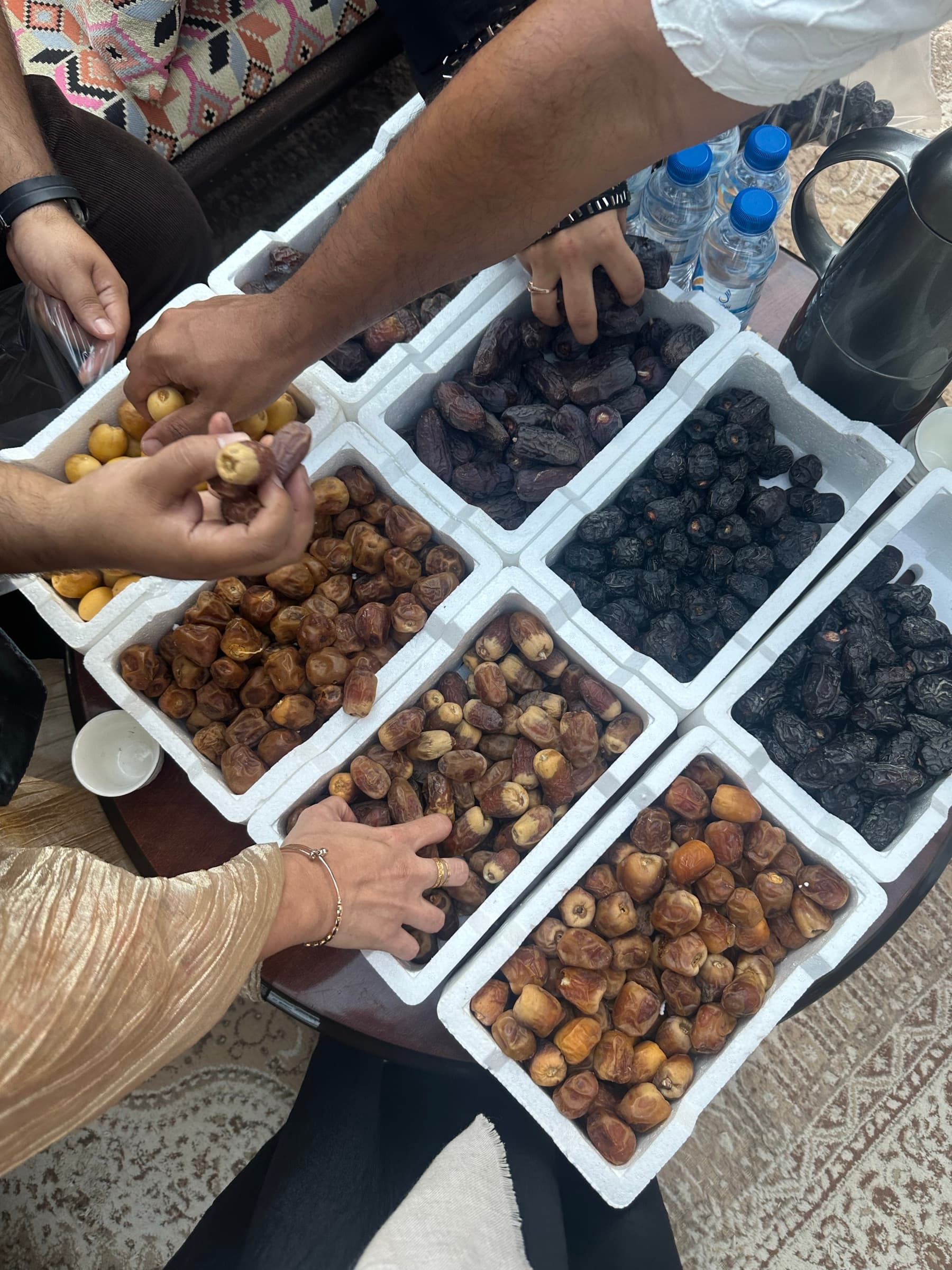 Hands reaching for a spread of dates and tea, shared among guests and hosts